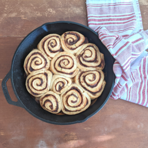 sourdough cinnamon rolls baked in a cast iron skillet on a farmhouse table