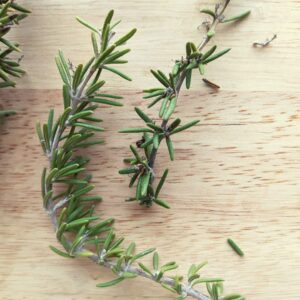 two rosemary sprigs on a wooden cutting board